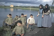 A group of children and two Grey Nun Sisters standing on the bank of the river. Fort Resolution, NWT, 1955. 